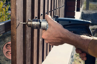 Hands of a fencing contractor holding a power tool working on a fence in Markham, Ontario.